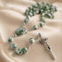 A green and white marbled rosary with a metal crucifix and oval centerpiece, on satin fabric.