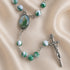 Rosary with green and white marbled beads, a silver-tone crucifix, and an oval medallion, on a beige satin fabric background.