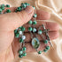 A close-up of a hand holding a green and white rosary with a silver crucifix and an oval centerpiece, on a soft beige satin.