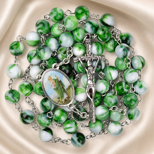 A green and white marbled rosary with a metal crucifix and an oval medallion, on a cream satin background.