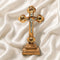 A frontal image of a hand-crafted small standing olive wood crucifix with halo and intricate details, featuring olive leaves, dried flowers, holy soil and incense on white background.