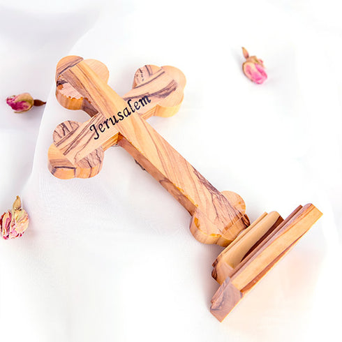 Image of a back of an hand-crafted small standing olive wood cross with petals around it, against white background.