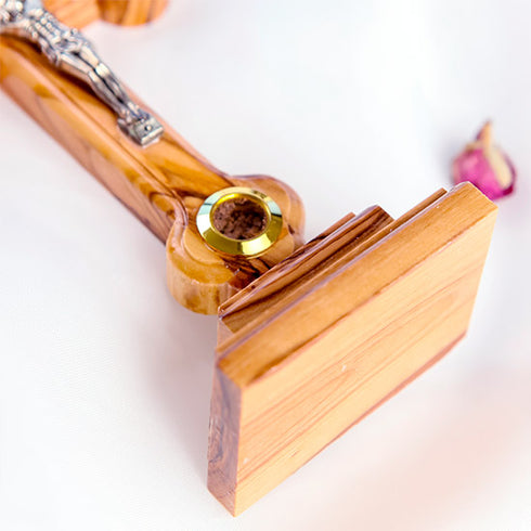 Detail of the bottom part of a hand-crafted standing olive wood crucifix with holy soil, against white background.
