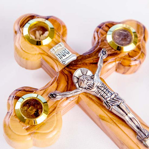 A pack shot of a detail on hand-crafted standing olive wood crucifix with halo and intricate details, featuring olive leaves, dried flowers, holy soil and incense, against a white background.