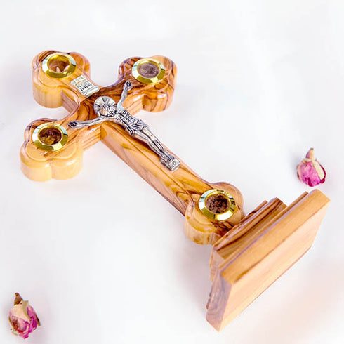 A hand-crafted small standing olive wood crucifix with halo and intricate details, featuring olive leaves, dried flowers, holy soil and incense.
