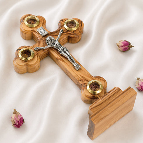 A hand-crafted small standing olive wood crucifix with halo and intricate details, featuring olive leaves, dried flowers, holy soil and incense.