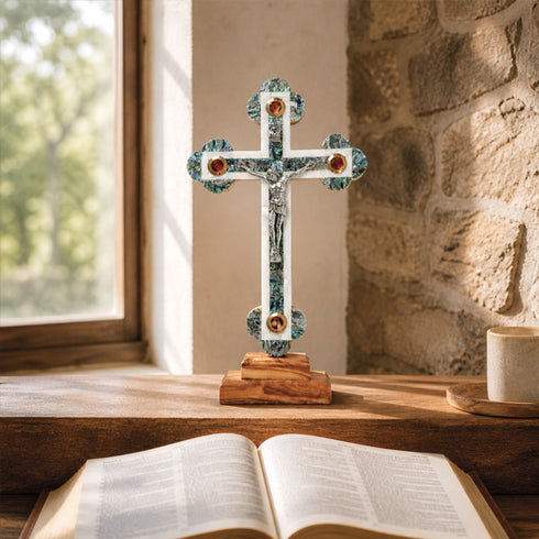 Decorative cross on a wooden surface with an open book in front, against a stone wall and window.