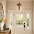Foyer with a wooden cross above a white door, vase with dried flowers, and mirror.