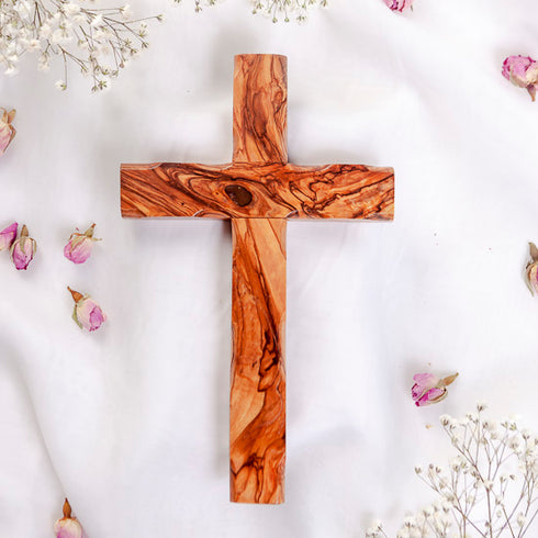 Handmade olive wood Thorn cross from Bethlehem, photographed on white surface with rose petals.