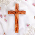 Handmade olive wood Thorn cross from Bethlehem, photographed on white surface with rose petals.