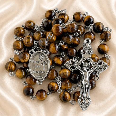 A rosary with polished brown tiger's eye beads, a silver-tone crucifix, and a central oval medallion with the text 'Ruega por Nosotros'.