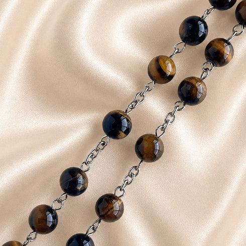 A close-up of a beaded chain necklace with polished tiger's eye beads in brown and black, separated by metal links.