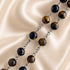 A close-up of a beaded chain necklace with polished tiger's eye beads in brown and black, separated by metal links.