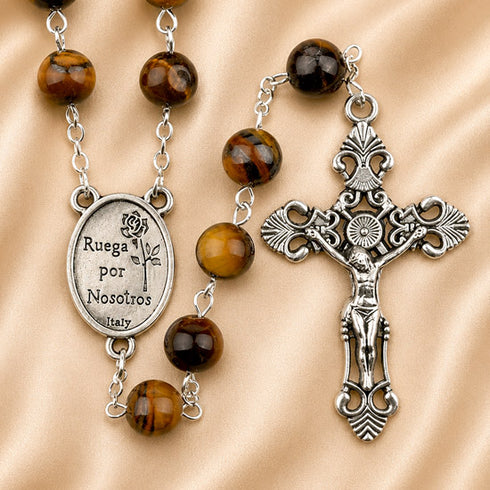 A rosary with brown tiger's eye beads, a silver-tone crucifix, and a medallion engraved with 'Ruega por Nosotros'.