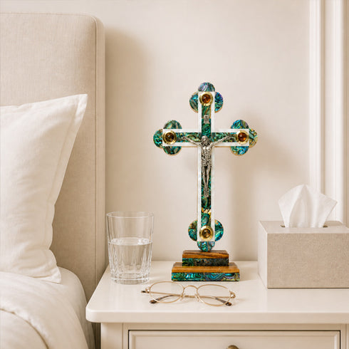 Decorative cross on a nightstand next to a glass of water and a box of tissues.