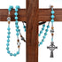 Turquoise beaded rosary with a silver cross hanging on a wooden cross