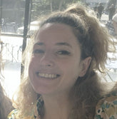 Woman with curly hair smiling outdoors, with a blurred background