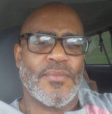 Older African guy with glasses sitting in a car.