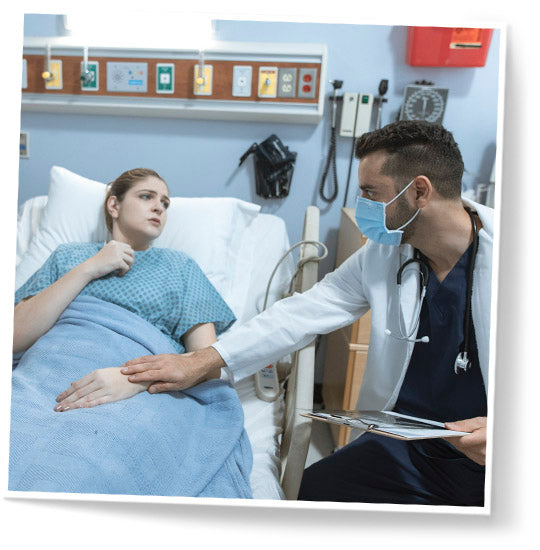 Woman laying in a hospital bed and a male doctor with a mask, standing next to her, comforting and holding her hand.
