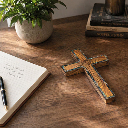 Wooden latin cross on a table next to a notebook and a plant