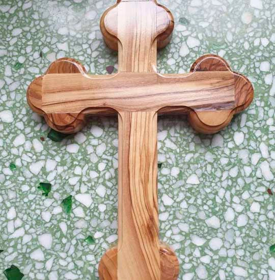 Orthodox Budded olive wood cross on green background.