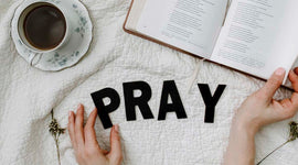 Open book, cup of coffee, and hands with 'PRAY' letters on a textured surface