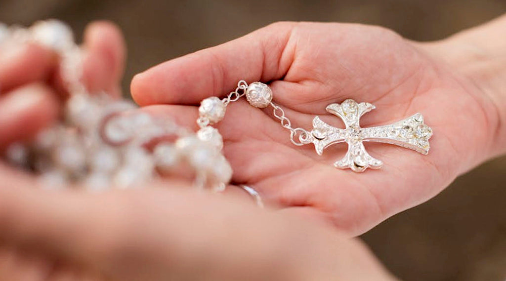 Hand holding a silver cross pendant with blurred background
