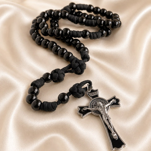 Black rosary knotted centerpiece and a silver-toned crucifix pendant, displayed on champagne satin fabric.