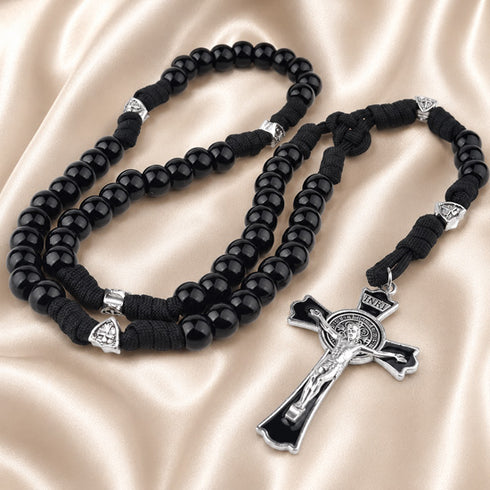 A black rosary with black cord and silver-tone metal accents, a crucifix, on a beige satin fabric background.