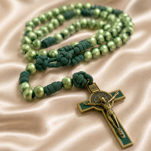 A green beaded rosary with knotted cords and a gold-toned crucifix, on a beige satin fabric.