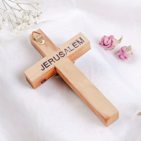 Back of a small olive wood Latin cross from Bethlehem with word "Jerusalem", laid on white surface with rose petals.