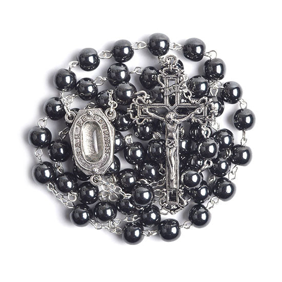 Black hematite rosary with a crucifix and Lourdes Holy Water medal on a white background.