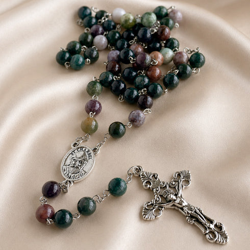 A rosary with multicolored stone beads, a silver-tone medallion, and a silver-tone crucifix, on draped satin fabric.
