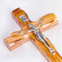 A handmade olive wood thorn cross with a crucifix, placed on a white surface with a few pink flowers scattered around.
