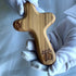 Olive wood comfort cross with the Piece of Holy Land logo, shown in hand with white glove