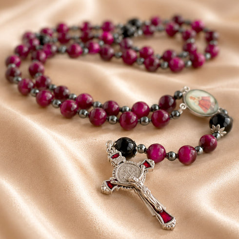 A rosary with red and black beads, a silver crucifix pendant, and a small medallion, on draped satin fabric.