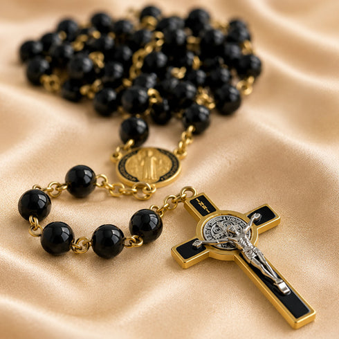 A close-up of a rosary with black beads, gold-tone chain links, a round gold medallion, and a cross with black inlay and a silver-toned crucifix.