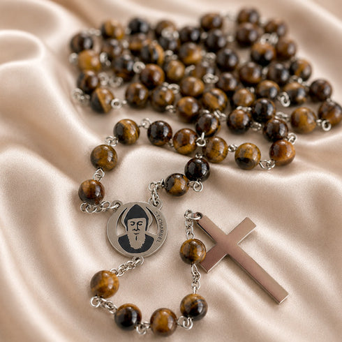 A rosary with tiger's eye beads, a round silver medal with St Charbel portrait, and a polished silver cross.