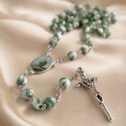 A green and white marbled rosary with a metal crucifix and oval centerpiece, on satin fabric.
