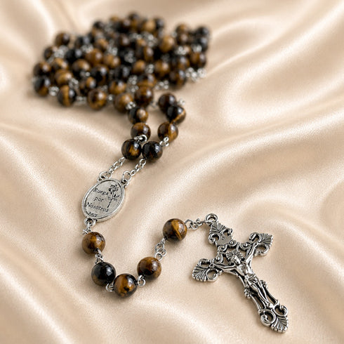 A Catholic rosary with brown and black tiger's eye beads, a silver-tone medal, and an ornate silver crucifix.