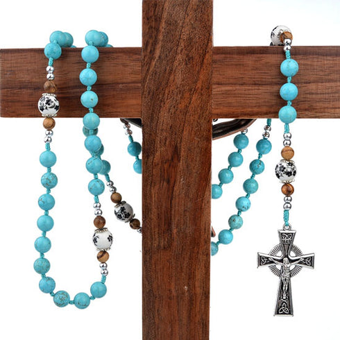 Turquoise beaded rosary with a silver cross hanging on a wooden cross
